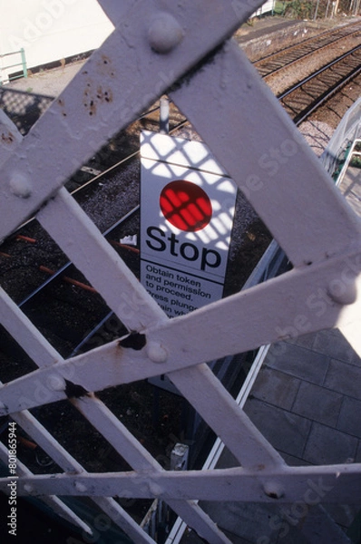 Fototapeta vertical image of grey crisscross metal guard rail on railway overpass walkway. red stop signage depicting danger. Location Woodbridge Railway station Suffolk UK 2003