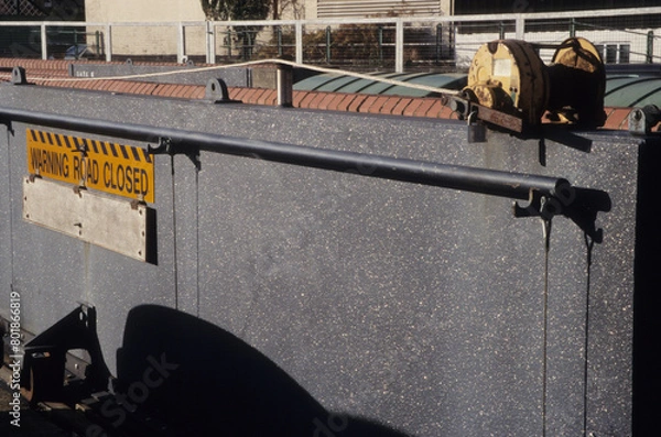 Fototapeta horizontal image of a solid metal walled barrier. Warning Road Closed sign on panel. Iron work pulley system. Padlock attached. closeup. Location Woodbridge Railway station Suffolk UK 2003