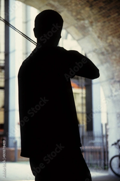 Fototapeta vertical image of a man playing his violin. busking under a stone arch. back view silhouette only visible. Location Thames Bank London UK 2003