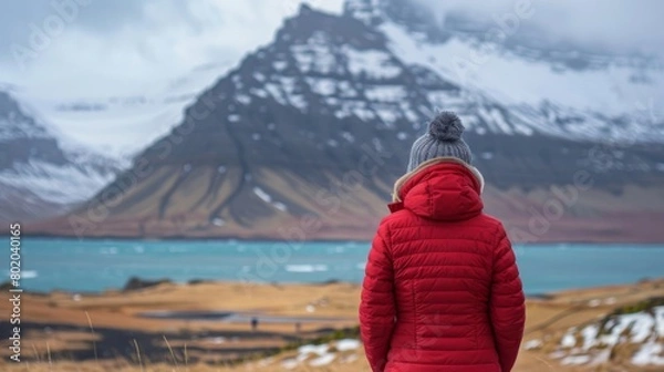 Fototapeta A woman in a red jacket standing in front of a mountain