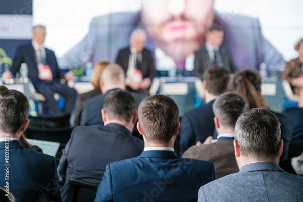 Obraz Focused audience listening to speaker at a corporate conference event. Business professionals engaged in a dynamic presentation, fostering networking and professional growth.