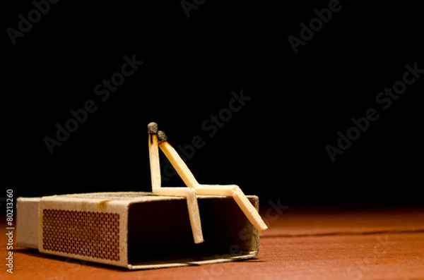 Fototapeta Two match humans sitting on matchbox on a dark background