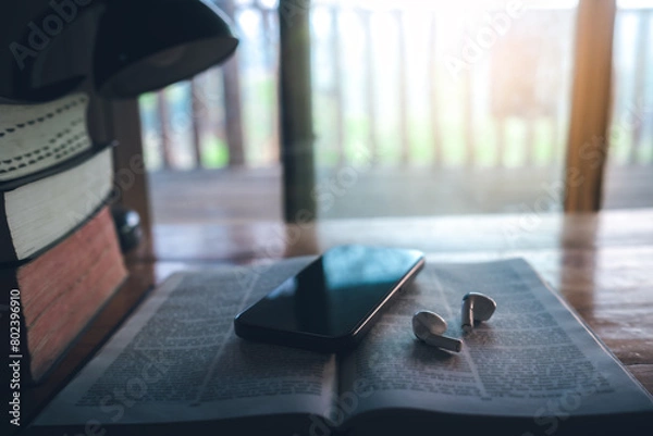 Fototapeta Bible and a smartphone with earphones on wooden table, Christian online technology concept, online live church for sunday service. holy bible book and online study.