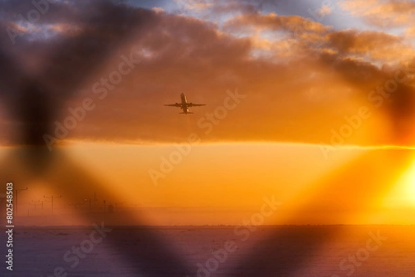 Fototapeta The silhouette of an airplane during takeoff in a protected area behind a fence. The concept of air travel bans. Sanctions in aviation