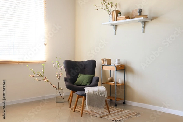 Fototapeta Stylish living room with black armchair, shelf and vase with blooming branches