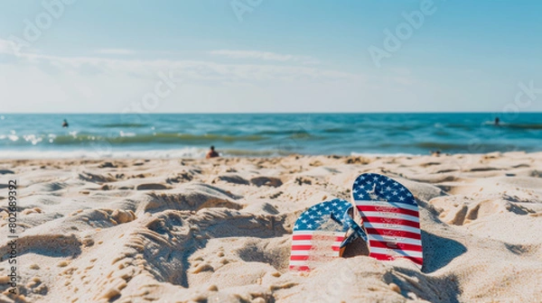 Fototapeta American flag flip flops on sandy beach with ocean backdrop