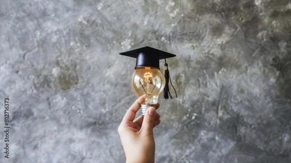 Obraz Hand holding lightbulb with graduation cap against textured background