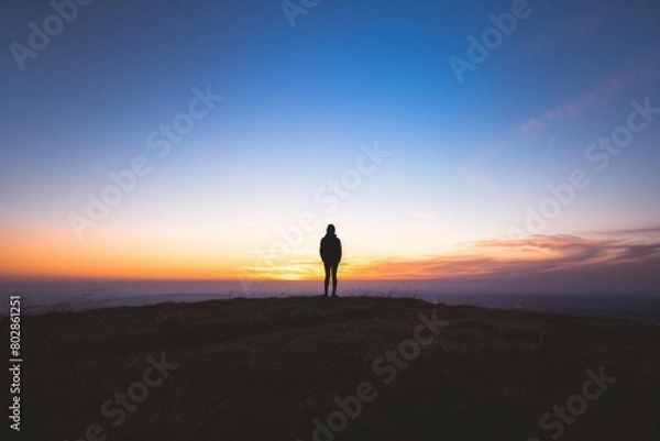 Obraz Step into the serene silhouette of a lone figure standing on a hilltop, watching as the sun sinks below the horizon and casts long, Generative AI