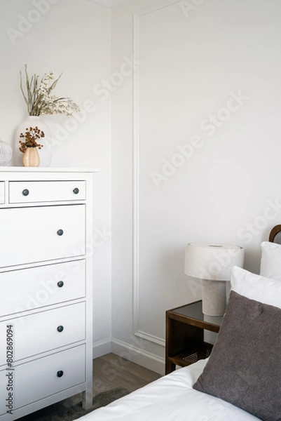Fototapeta Bedroom with white chest of drawers near comfort bed with lamp on side table