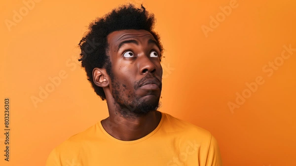 Fototapeta Portrait of a confused puzzled minded African American man in orange top isolated on orange background, with copy space