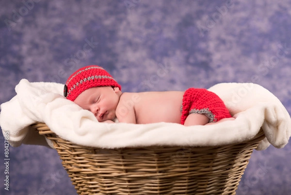 Fototapeta Newborn baby sleeping in a basket with purple background.