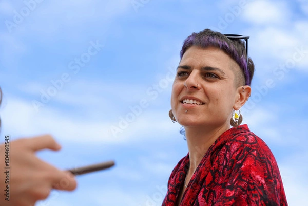 Fototapeta Portrait of a authentic woman with purple hair with a blue sky talking with a friend in summertime