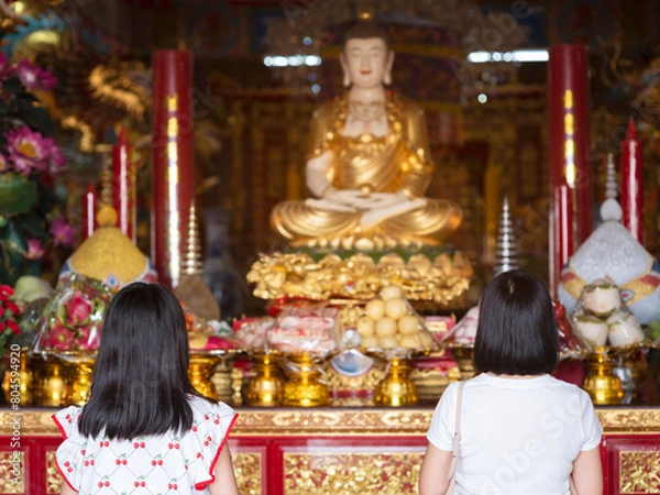 Fototapeta Daughter and mother pay respects to Buddha statue in Chinese shrine