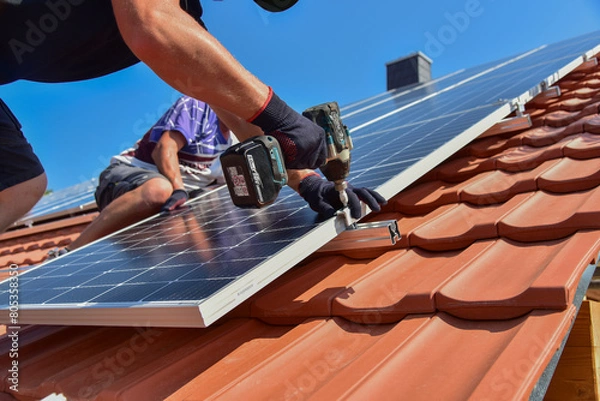 Obraz Dachdecker beim Aufbau einer Photovoltaikanlage auf einem neu gedeckten Ziegeldach: Verschraubung der Solarmodule an den Endklemmen des Schienensystems am Dachrand