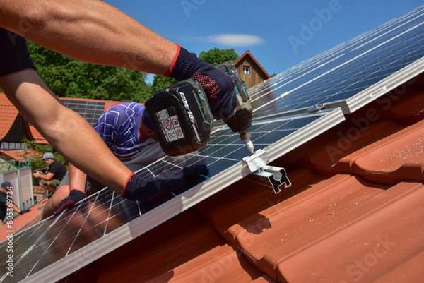 Obraz Dachdecker beim Aufbau einer Photovoltaikanlage auf einem neu gedeckten Ziegeldach: Verschraubung der Solarmodule an den Endklemmen des Schienensystems am Dachrand