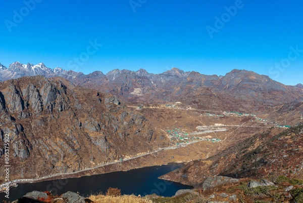 Obraz In the Himalayas, a lake winds through a canyon surrounded by towering mountains. The rugged terrain, clear sky, and pristine water create a breathtaking natural landscape in this highland region.