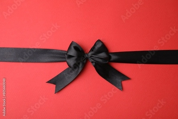 Fototapeta Black satin ribbon with bow on red background, top view