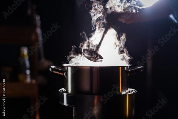 Fototapeta A boiling pot steams up as a chef uses a ladle to stir soup in a cooking pot in a restaurant.