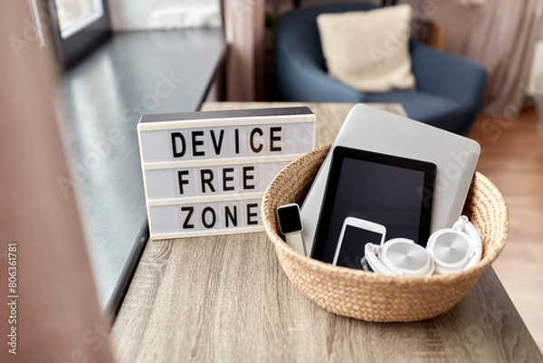 Fototapeta digital detox and technology concept - close up of device free zone words on light box and different gadgets in wicker basket on table at home