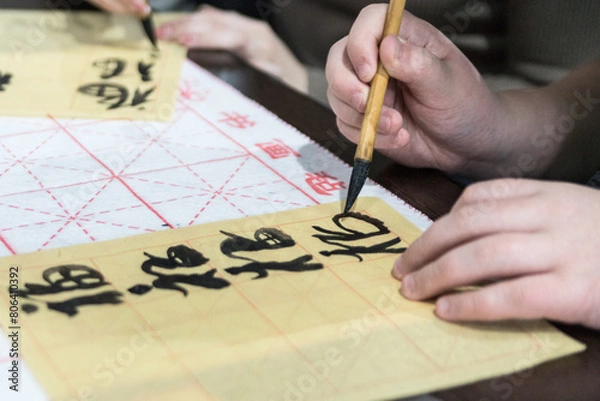 Fototapeta Chinese Calligraphy. Female hand with Asian hieroglyphs, brush and on wooden background, closeup.