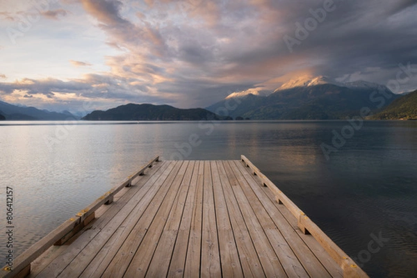 Fototapeta Wooden boat dock leading out to a lake with calm waters with a sunset sky. Harrison Lake, east of the lake are the Lillooet Ranges while to the west are the Douglas Ranges, British Columbia, Canada. 