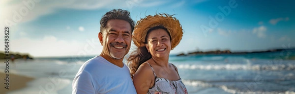 Obraz Portrait of Happy Hispanic latin retired senior couple on a sunny tropical beach with beautiful water waves during the day smiling, wide banner with copyspace