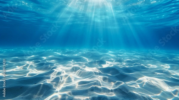 Fototapeta Underwater view with bright sunlight streaming through blue water onto a sandy bottom.