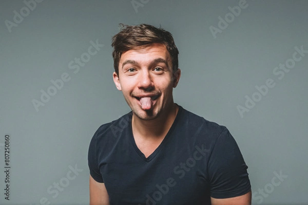 Fototapeta Waist portrait of a young handsome man on a gray background. A man shows his tongue