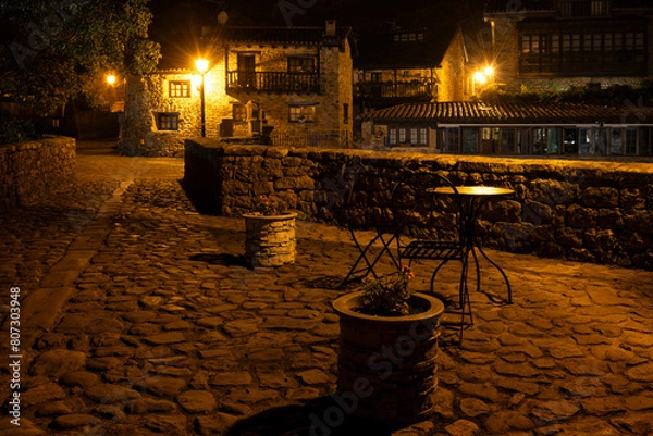 Obraz A stone walkway over the old bridge with a few tables and potted plants. The scene is quiet and peaceful at night. Barcena Mayor, Saja-Besaya Natural Park, Cantabria, Spain
