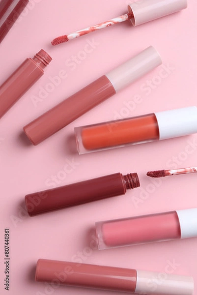 Fototapeta Different lip glosses and applicators on pink background, flat lay