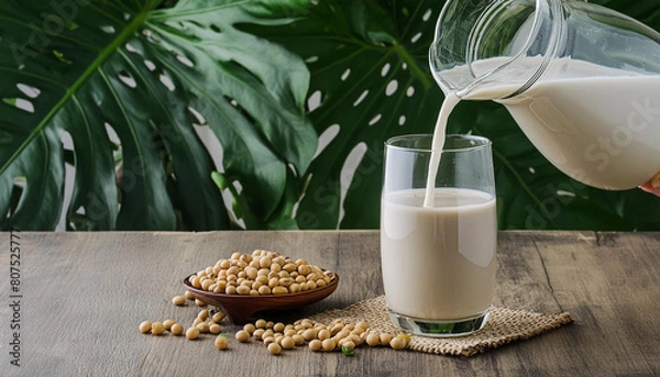Obraz Pouring soy milk in a glass with soy beans on wooden table