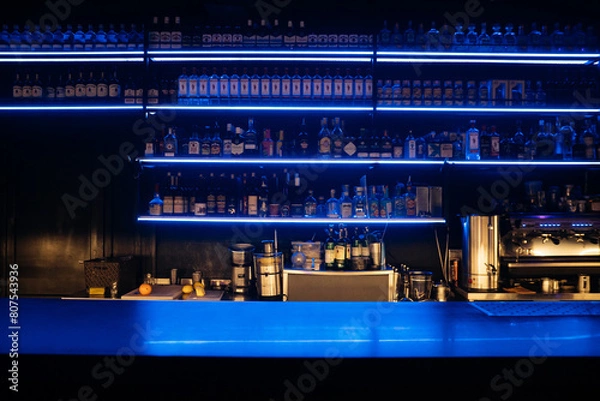 Fototapeta A bar with a blue counter and shelves of liquor. The bar is empty and the lights are on.