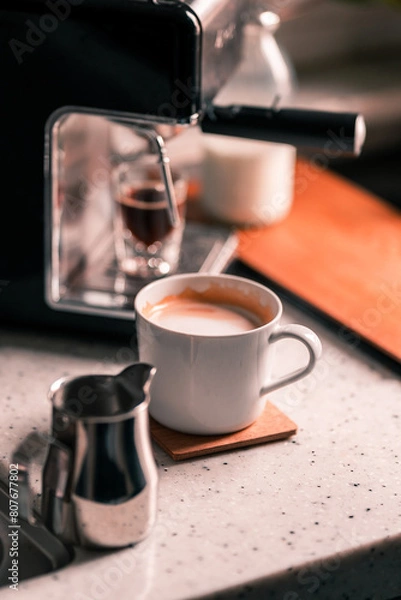 Obraz A glass of caffe latte with home coffee machine with a shot glass of espresso in the background