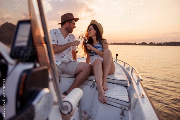 Obraz Couple making a toast and drinking champagne while sailing to the sunset on a boat