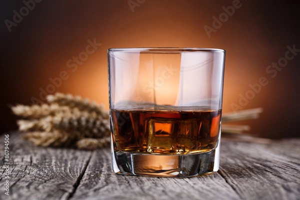 Fototapeta Glass of whiskey with ice and wheat on a wooden table.