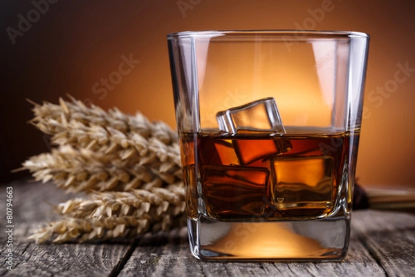 Fototapeta Glass of whiskey with ice and wheat on a wooden table.