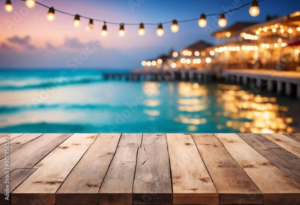 Fototapeta Seaside Serenity, Wooden Table Overlooking Beach Cafes with a Dreamy Bokeh Lights Background
