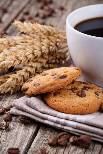 Fototapeta Cup of coffee with cookies and wheat on a wooden table.