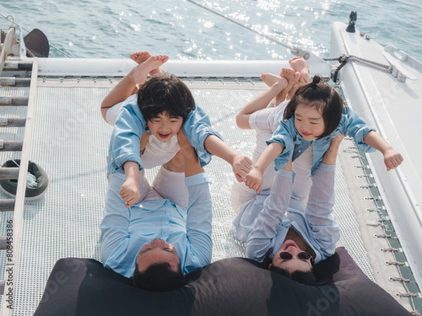 Fototapeta Happy Asian family relaxing, sitting, and playing on the polyester net of a luxury yacht during a sailing trip on the sea, enjoying the summer holiday concept.