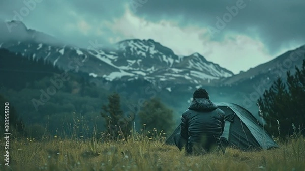 Fototapeta A dark-skinned person camped in the grass with a mountain backdrop.