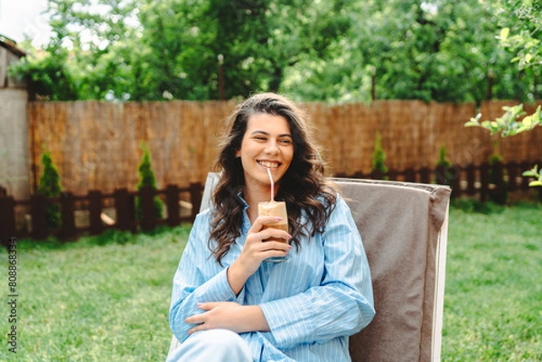 Fototapeta One young caucasian woman is relaxing on easy bed while drinking cold coffee in her backyard	