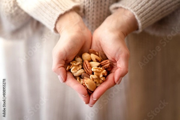 Fototapeta A mixture of different nuts in the hands of a woman. Handful of different nuts in hands in the shape of a heart