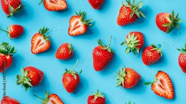 Fototapeta Detailed top view of strawberries and slices creatively arranged into a playful pattern on a cyan blue backdrop, isolated
