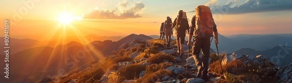 Obraz A group of people hiking up a mountain trail together, reaching the summit as the sun sets