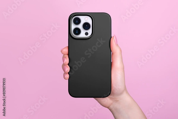 Obraz iPhone 15 Pro in female hand in black silicone cover isolated on pink background, phone case mock up back view