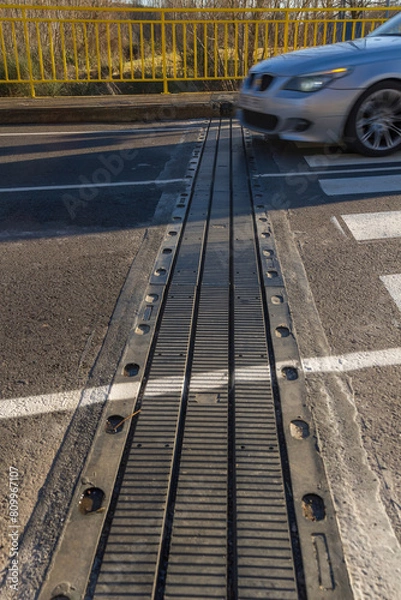 Fototapeta Car crossing an expansion joint in the asphalt of the road on a bridge
