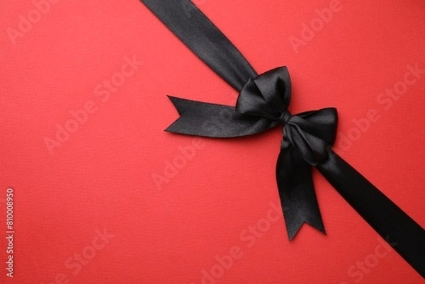 Fototapeta Black satin ribbon with bow on red background, top view. Space for text