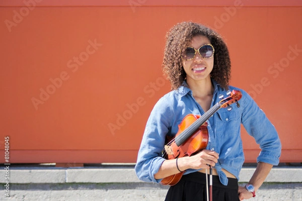 Fototapeta Female violinist with violin under arm smiling at camera