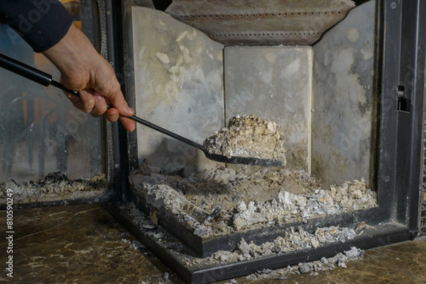 Fototapeta Cleaning the fireplace. Ash and charred piece of wood lying on the blade with a long handle closeup