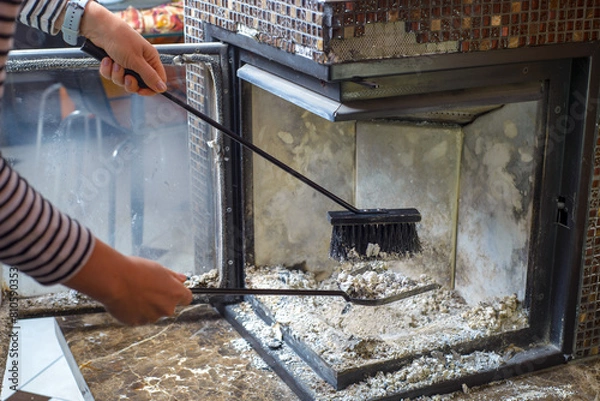 Fototapeta Cleaning the fireplace. Ash and charred piece of wood lying on the blade with a long handle closeup